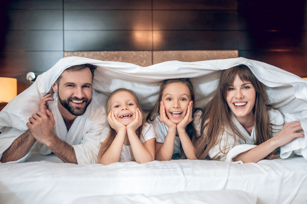 divertido-familia-sonriente-en-tunicas-blancas-acostado-en-la-cama-y-divertirse